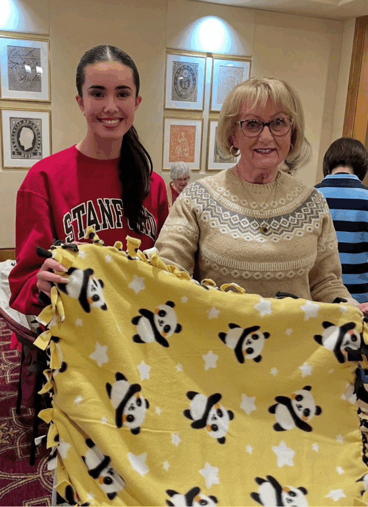 A high schooler and a resident show off the cute panda patterned blanket they made for shelter animals