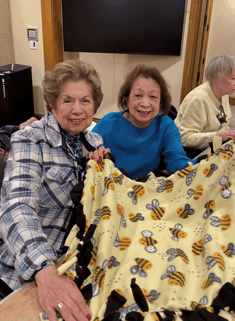 Two women pose for a photo with a blanket they made for shelter dogs